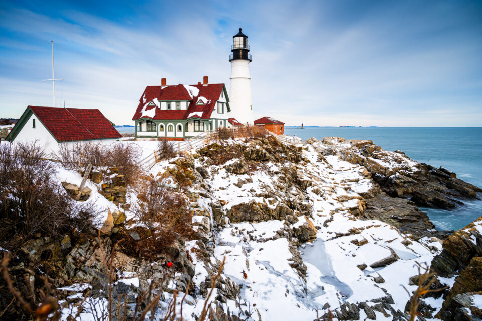 Portland Head Light stands proudly amidst a rocky, snow-covered coastline, framed by a crisp winter sky and the vast Atlantic Ocean.