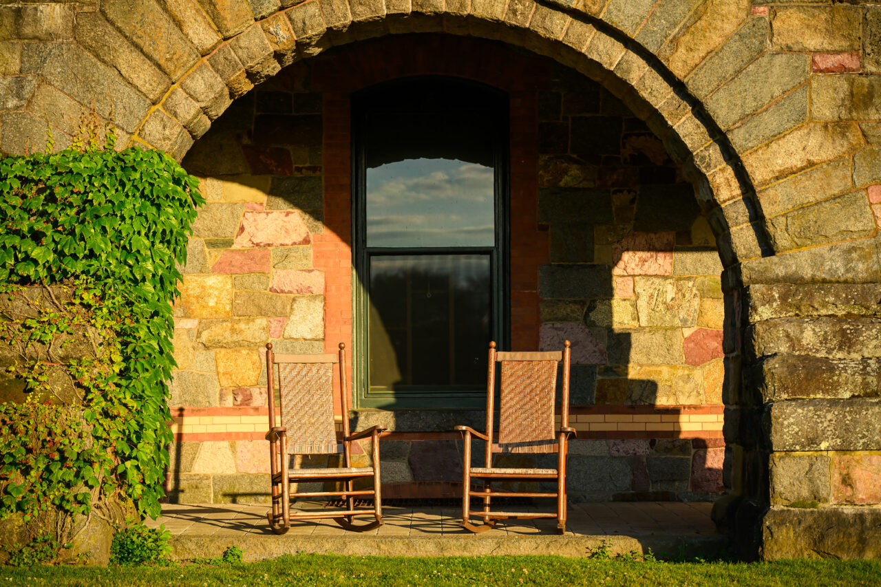 Two sunlit rocking chairs outside the Eustis Estate Museum in Milton, Massachusetts.