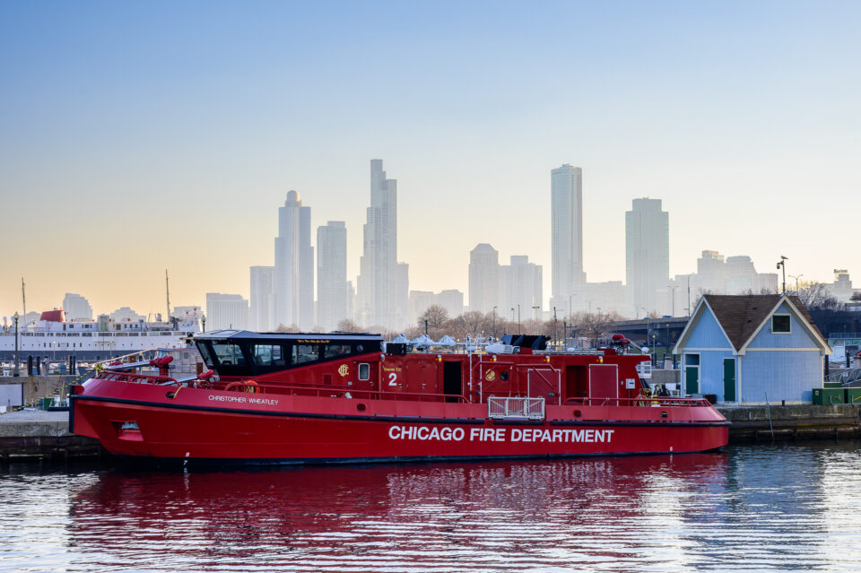 The Christopher Wheatley Fire Boat silhouetted against the Chicago skyline, with the city's iconic buildings in the background.