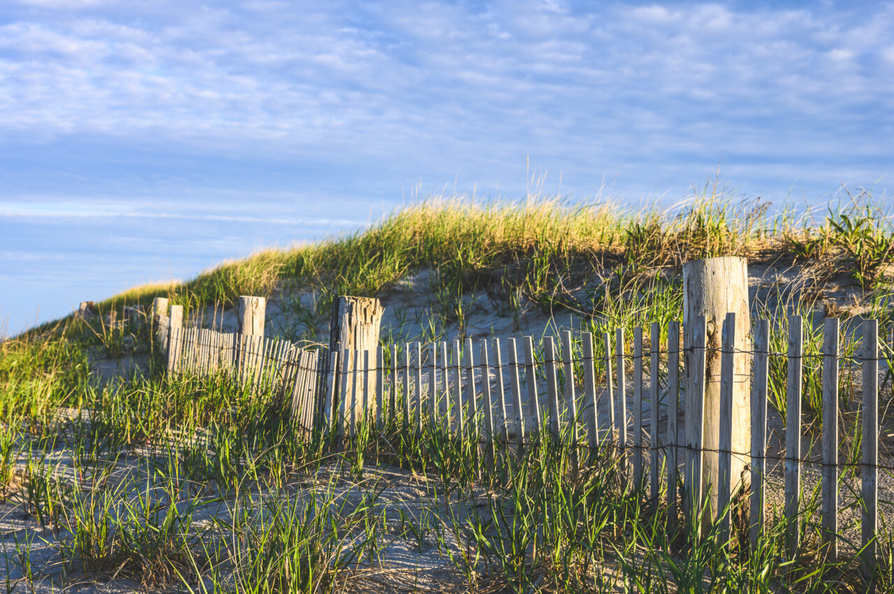 A fence leading to the sky filled with soft hues during sunset at Duxbury Beach.