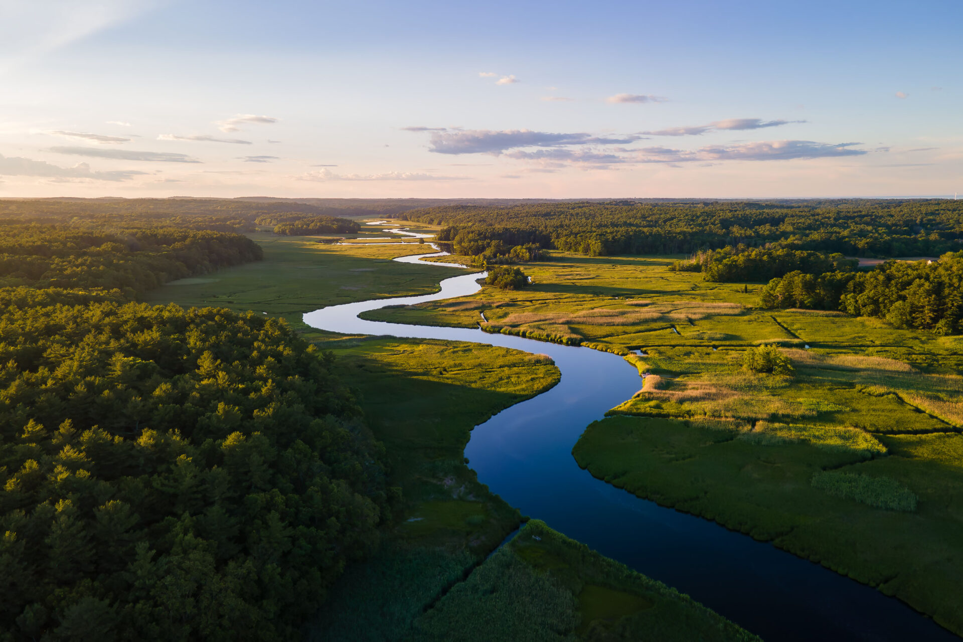 Aerial view of the North River at Route 3, winding through green salt marsh at golden hour.