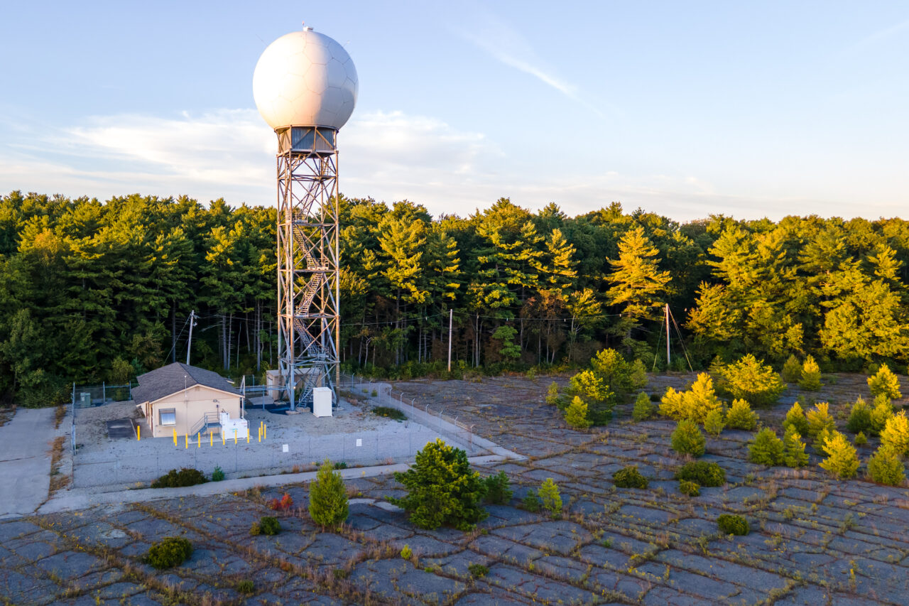 Aerial close-up of the white radar tower at South Weymouth Air Station over cracked concrete.