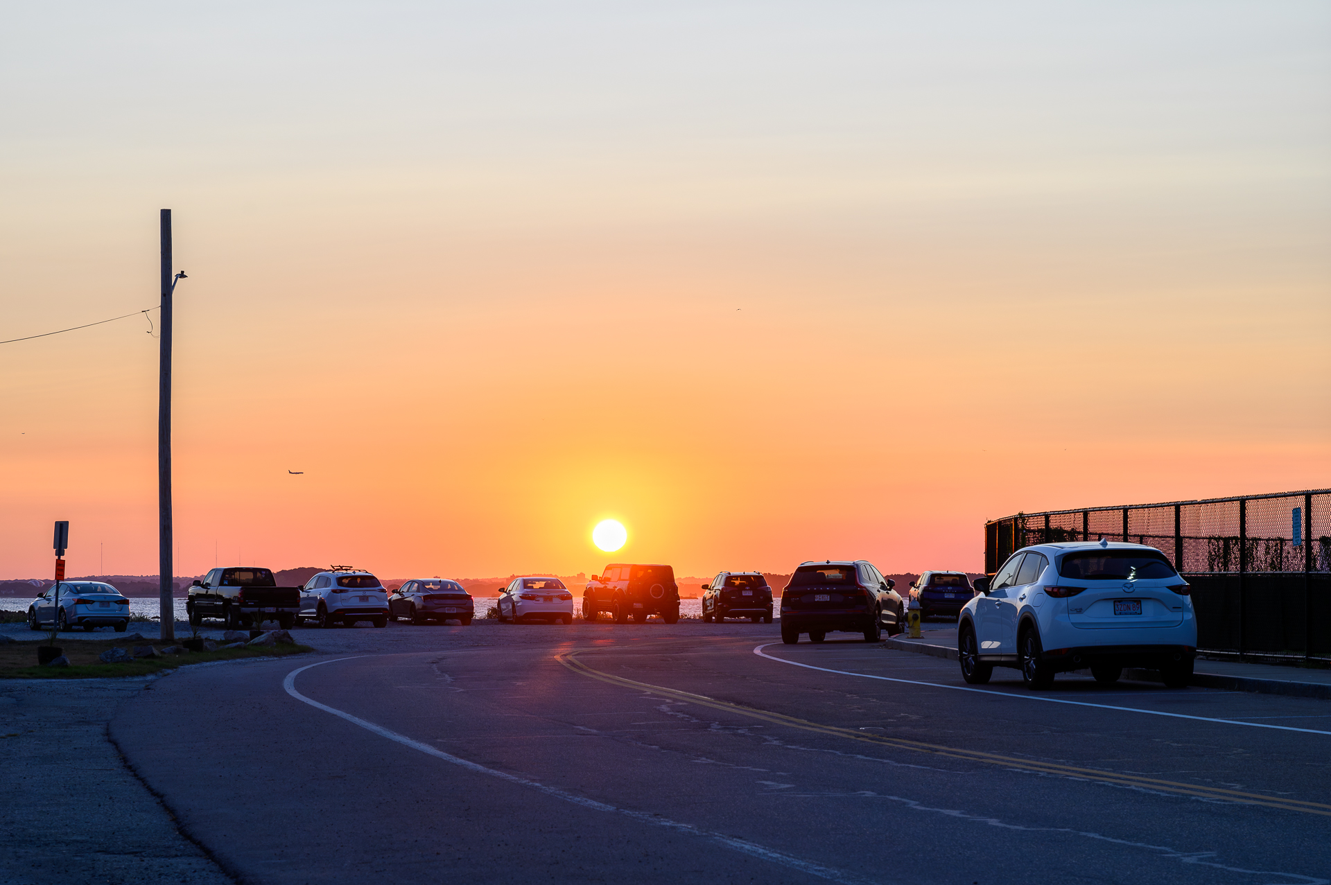 A row of cars parked as their owners sit and enjoy the sunset.