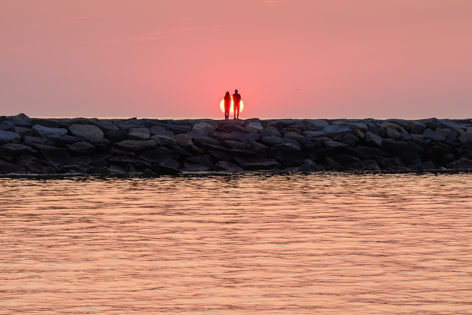 A couple framed directly in front of the sun rising over the horizon at Scituate Lighthouse.