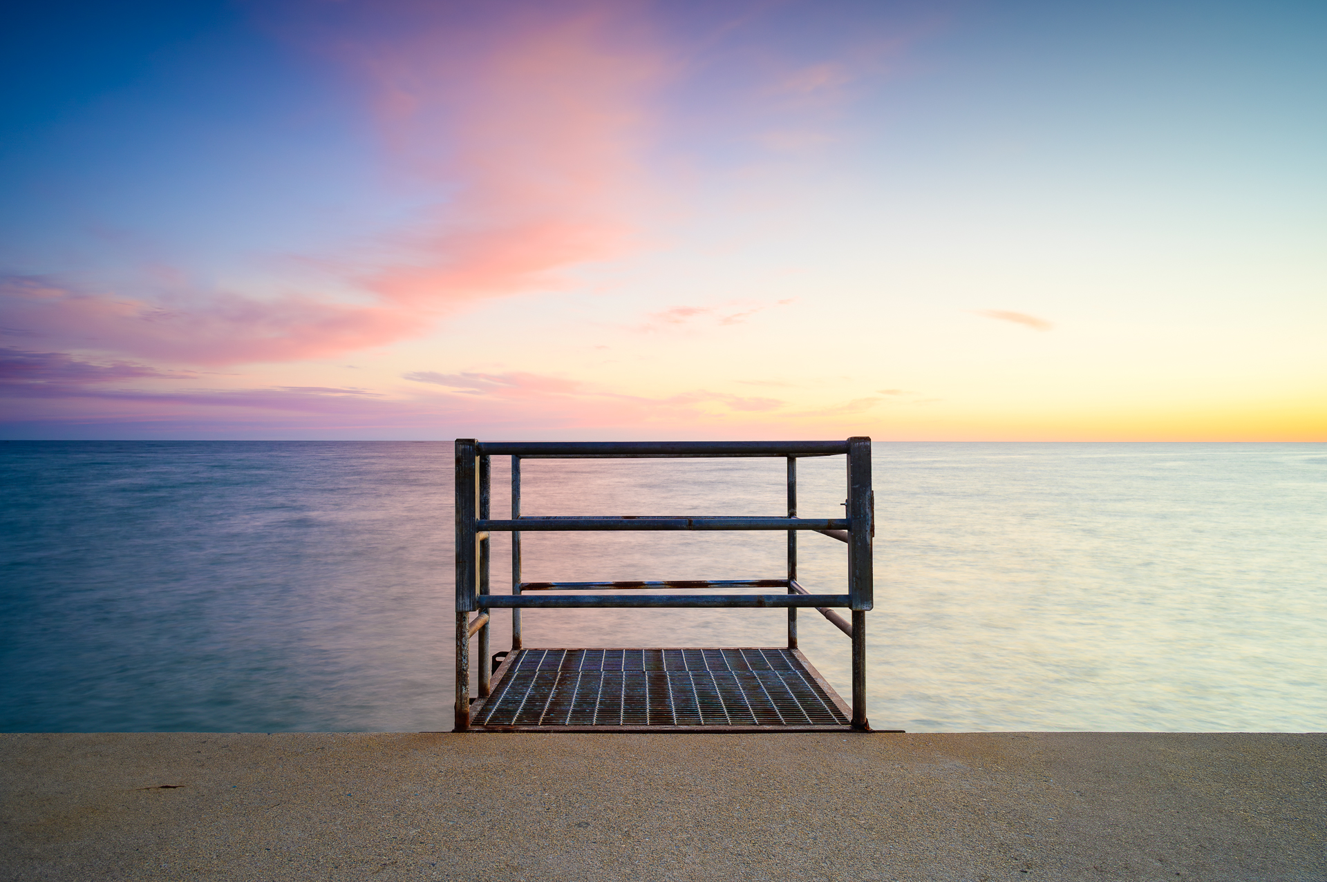 A colorful horizon beyond the rail of a platform by the seawall.