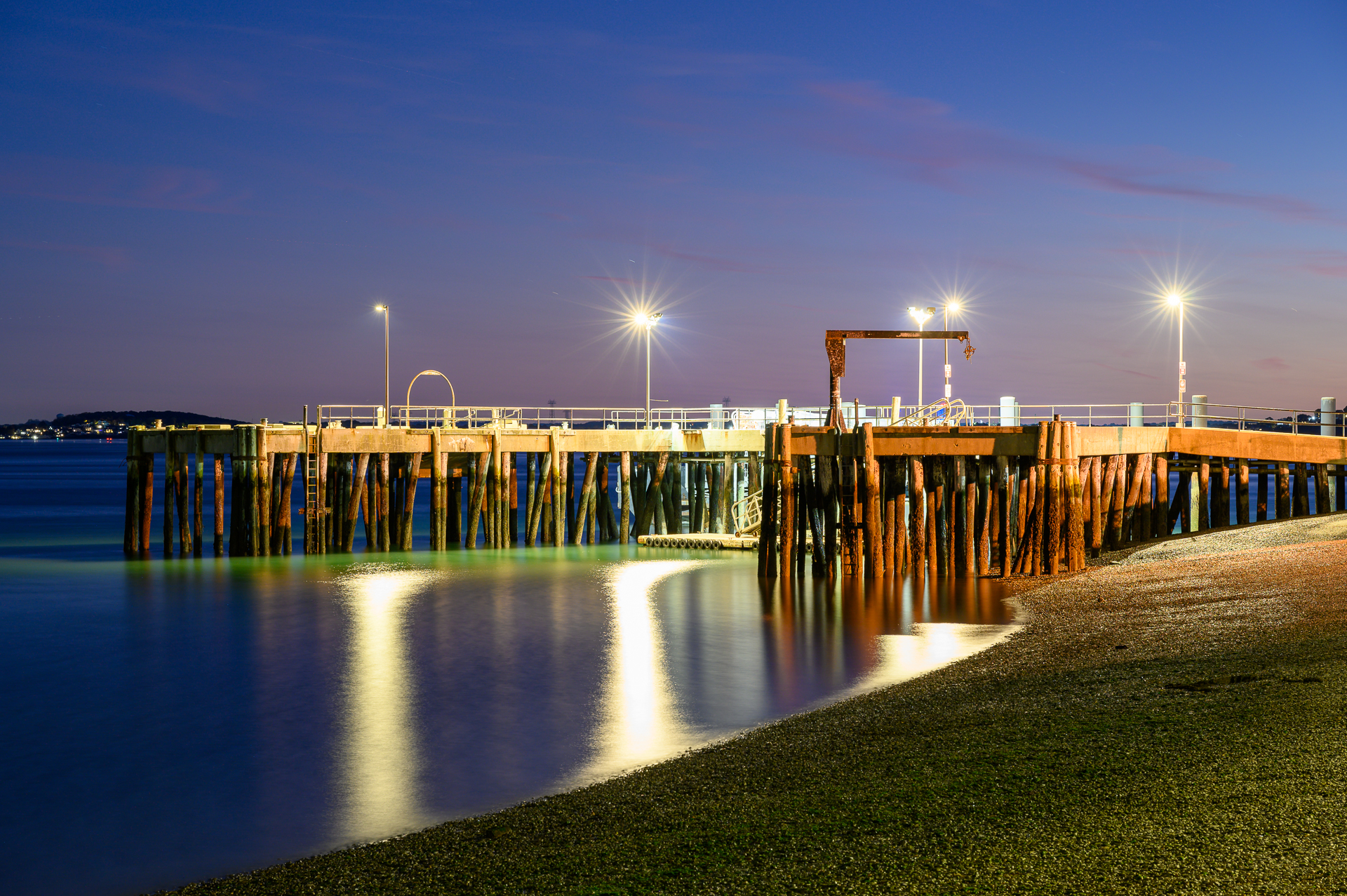 Long exposure of a pier at dusk with starburst lights, resembling pier stars, reflecting on the water.