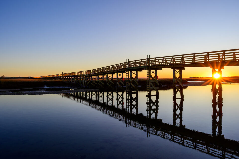 The Sandwich Boardwalk reflecting in the water at sunrise in Sandwich, Massachusetts.