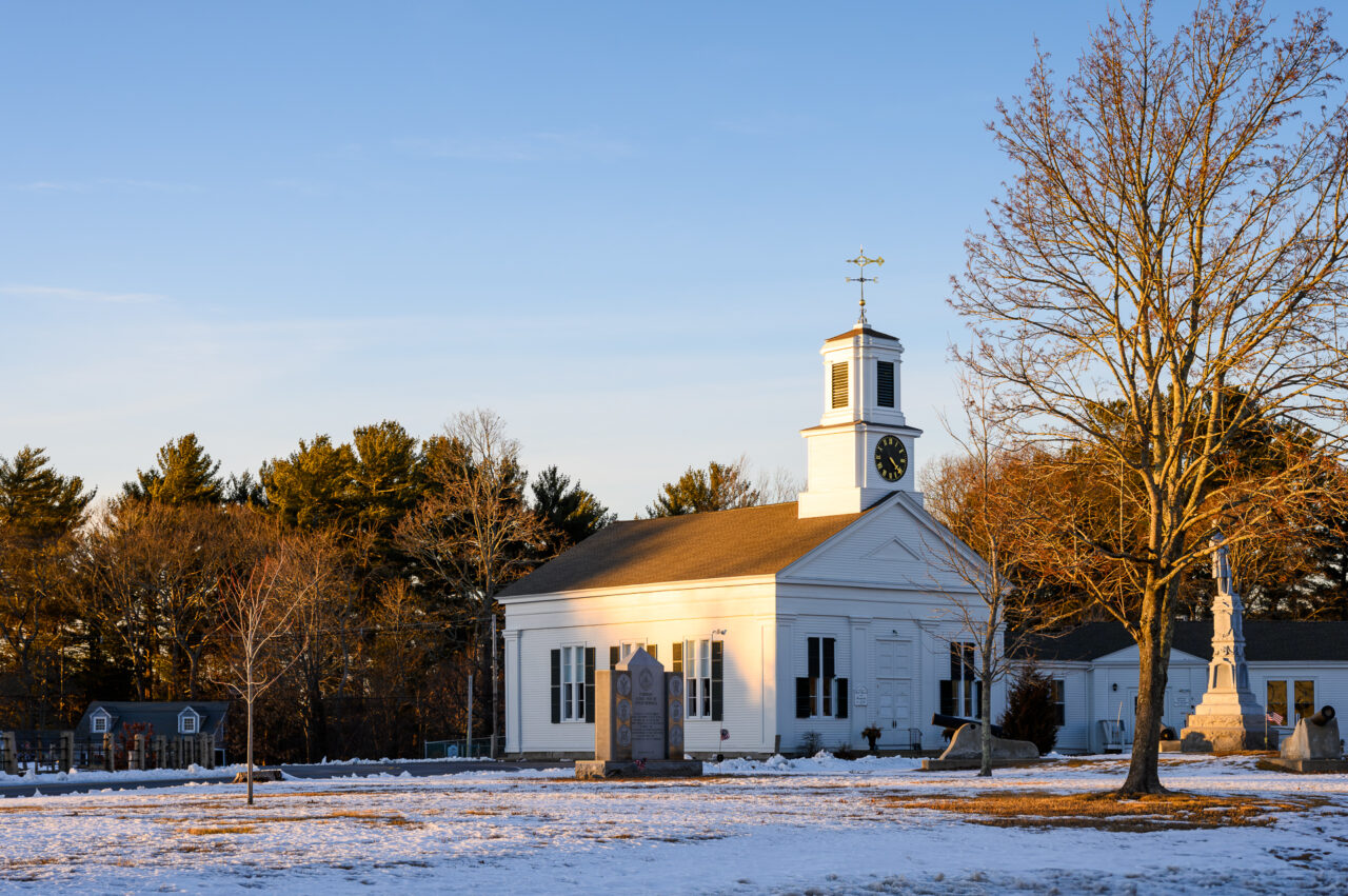 First Church in Pembroke in winter, with snow on the ground and warm sunlight on its white exterior.