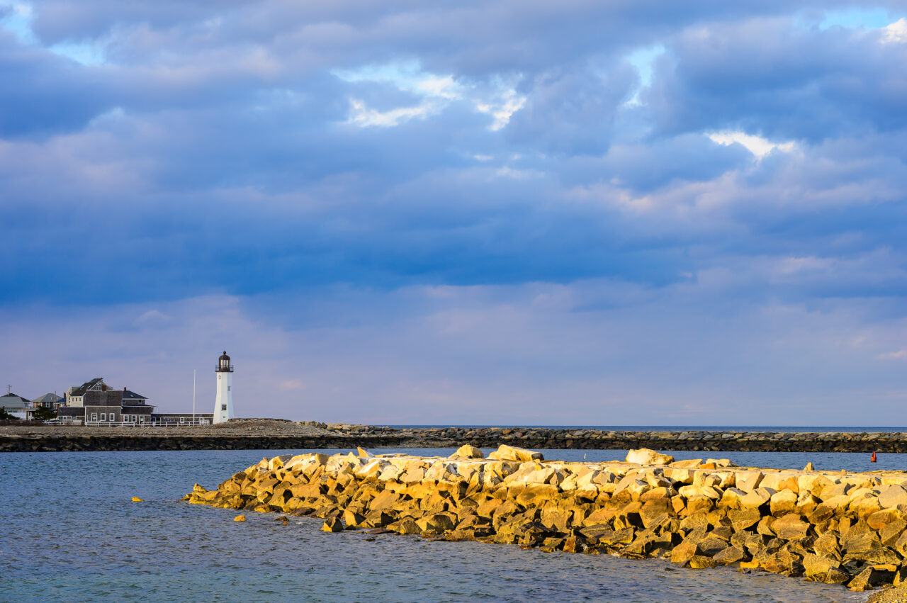 Dramatic storm clouds filled the sky over Scituate Lighthouse, with a small break allowing the sun to shine through, illuminating the nearby jetty.