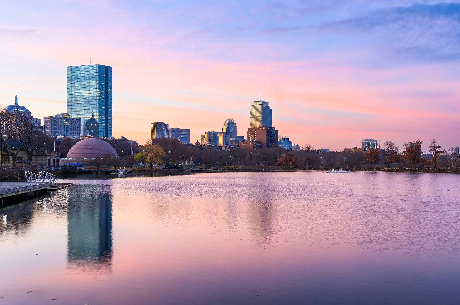 Charles River Esplanade bathed in soft morning light with the Boston skyline rising in the distance, silhouetted against a cotton candy sky.