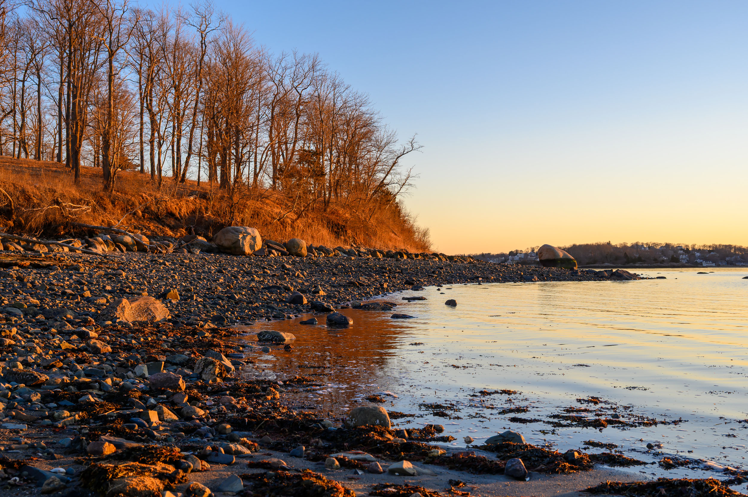 Warm evening light on the rocky shoreline at The Bar, with calm coastal waters at World's End in Hingham, Massachusetts.