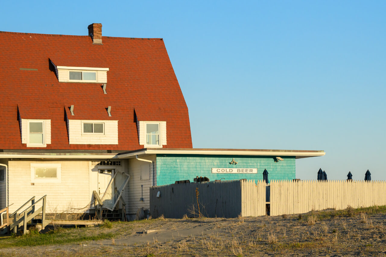 A Cold Beer sign hangs outside a beachside bar in the late afternoon light in Hull, Massachusetts.