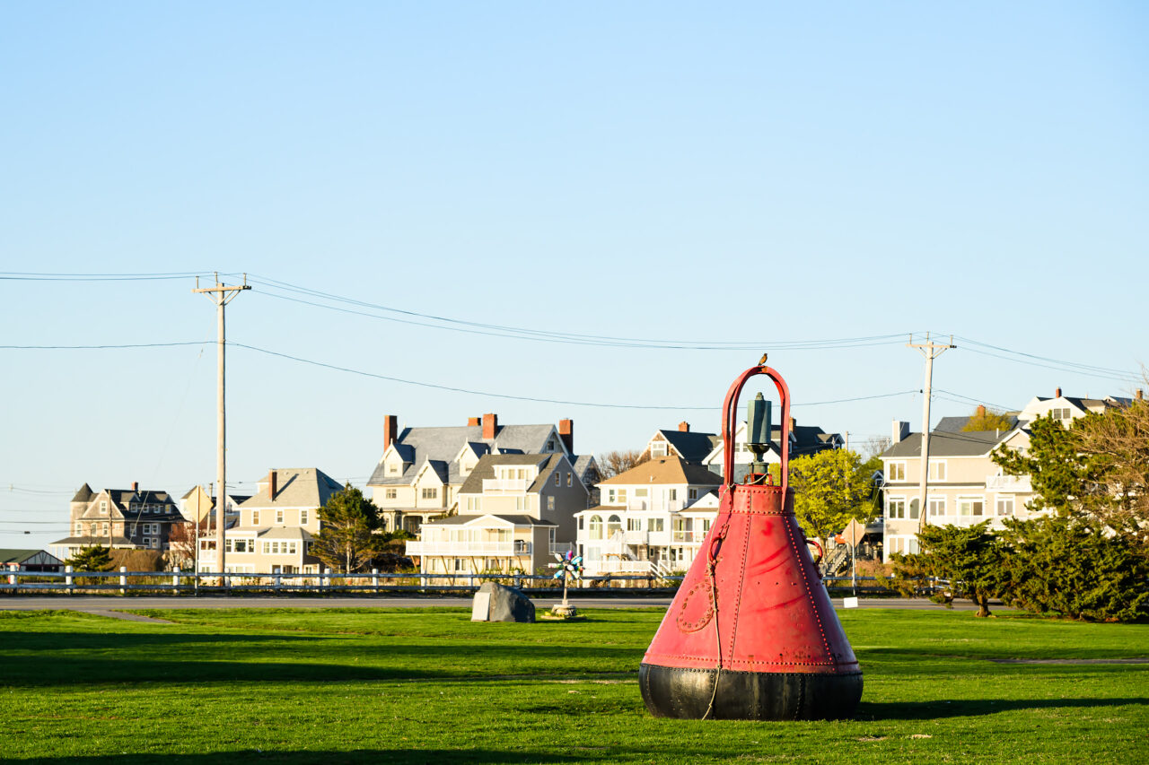 A red buoy sits on a lawn outside a Yacht Club in Hull, Massachusetts, marking its entrance during the late afternoon.