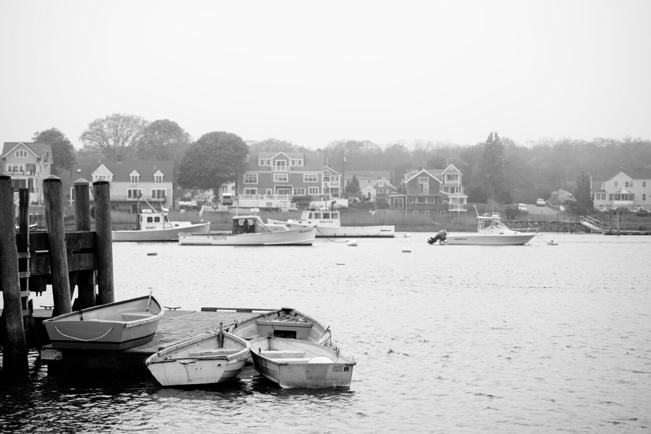 A group of small dinghies tied up at Marshfield Town Pier, seen during high tide with light fog in the harbor.