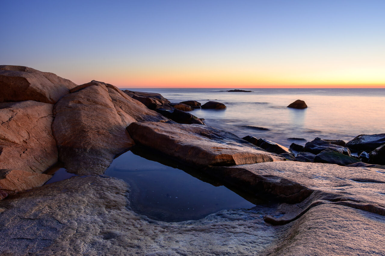Granite rocks and a reflective tide pool glowing in the warm light of a Scituate Neck sunrise.