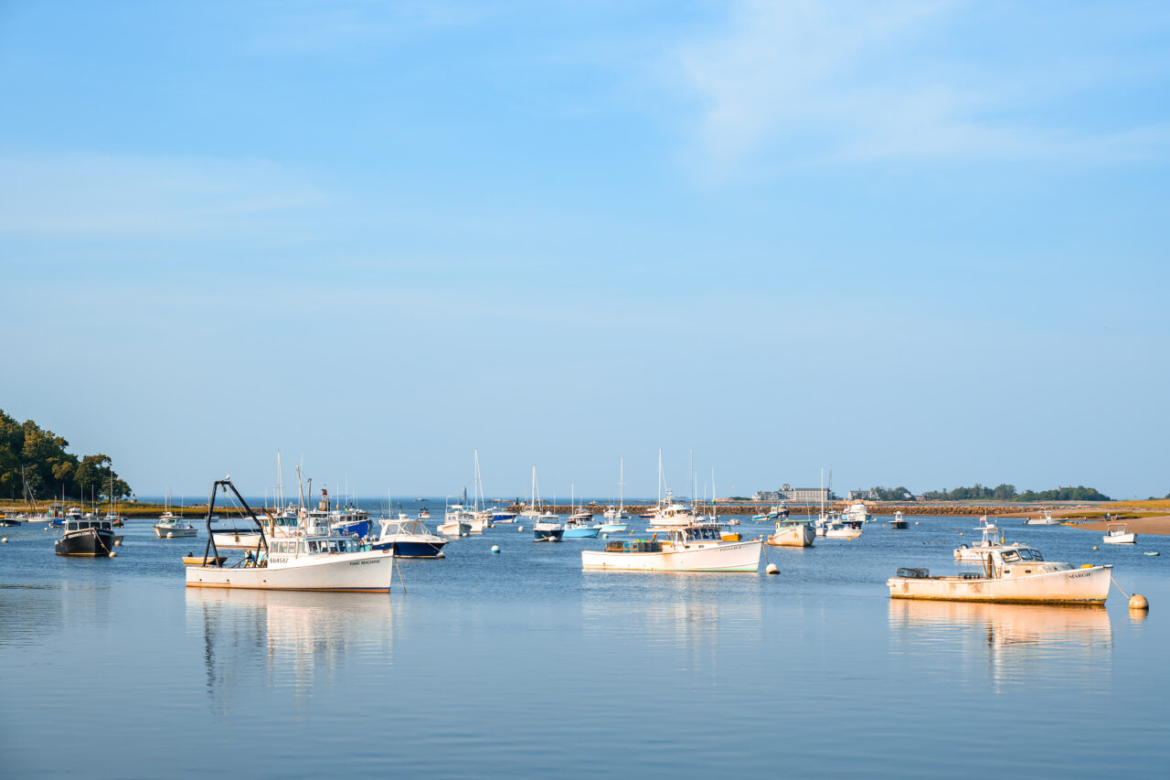Fishing and lobster boats anchored in Cohasset Harbor under clear afternoon skies.