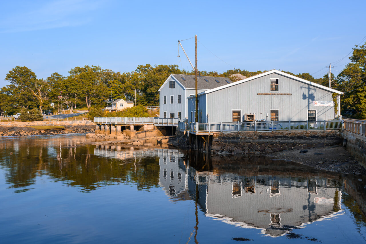 Historic Cohasset Lobster Pound building reflected in the harbor at high tide during golden hour.