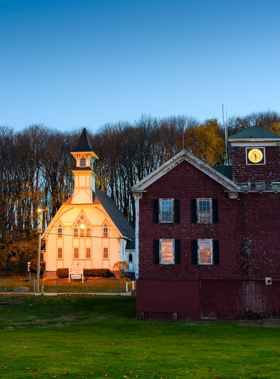 The First Town Hall in Hull, Massachusetts, with its white clocktower and red siding, seen in soft early morning light. Built in 1848, it once served as a school and meeting hall.
