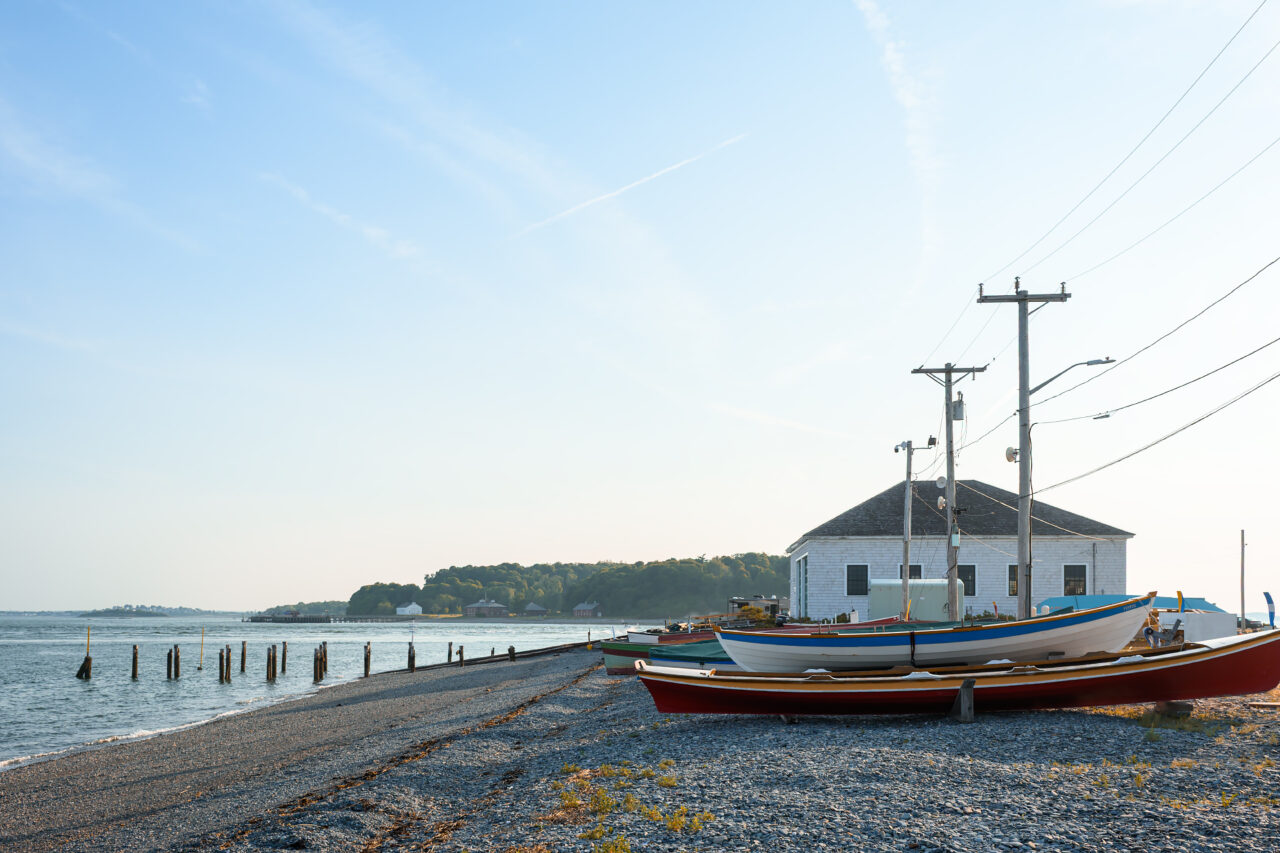 Several brightly colored wooden dory boats resting on a pebbly beach at Pemberton Point, Hull, Massachusetts.