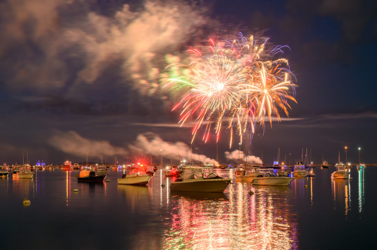 Colorful fireworks illuminating the night above boats anchored in Plymouth Harbor on Independence Day.