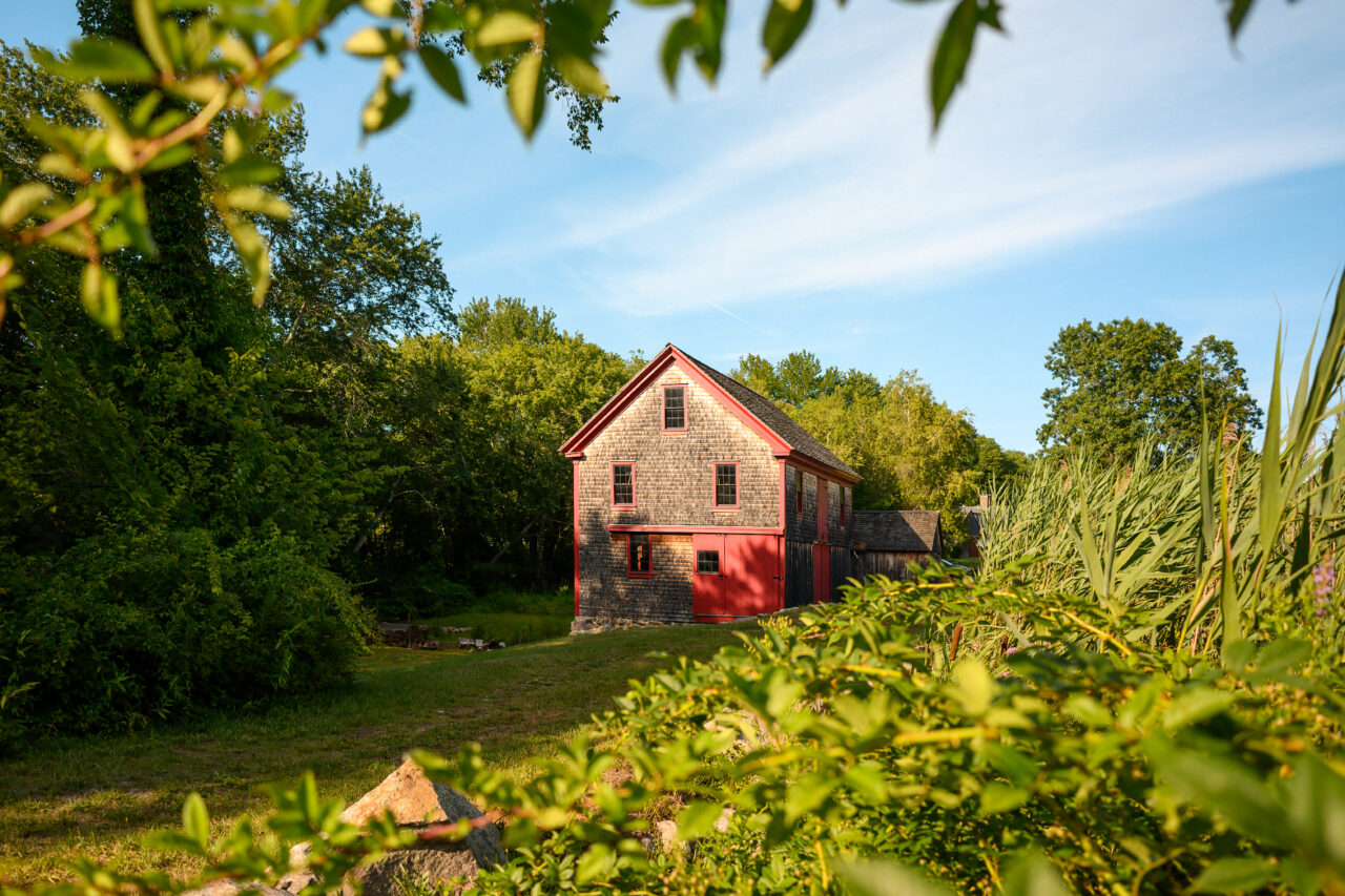 Hatch Mill in Marshfield, Massachusetts, a historic water-powered mill, framed by green trees and foliage under a blue sky.