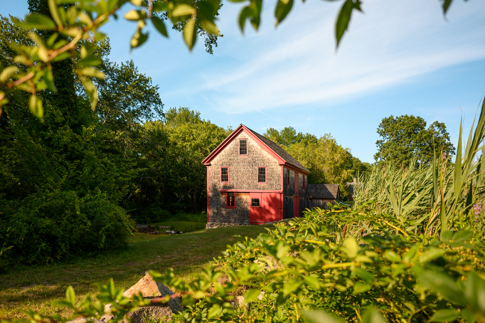 Hatch Mill in Marshfield, Massachusetts, a historic water-powered mill, framed by green trees and foliage under a blue sky.