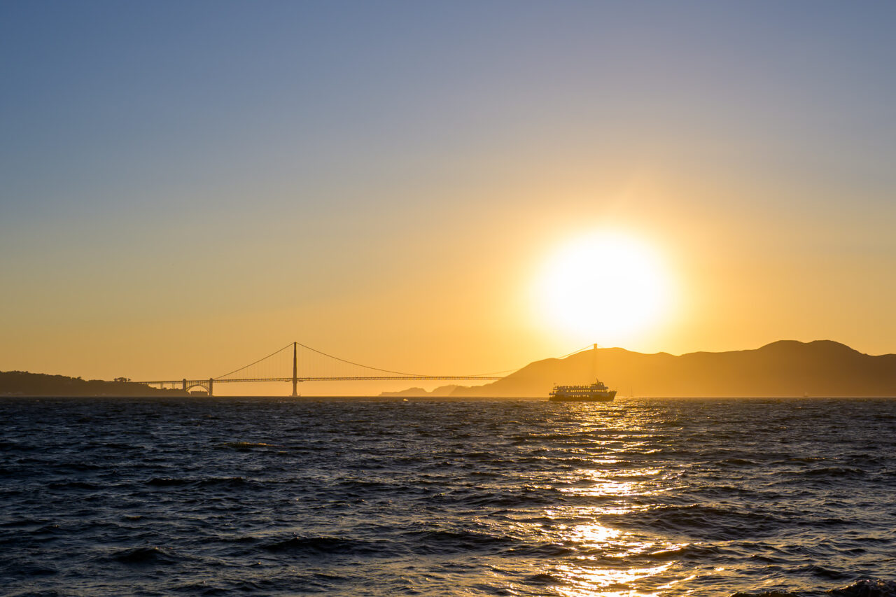 A ferry sails near the Golden Gate Bridge at sunset.