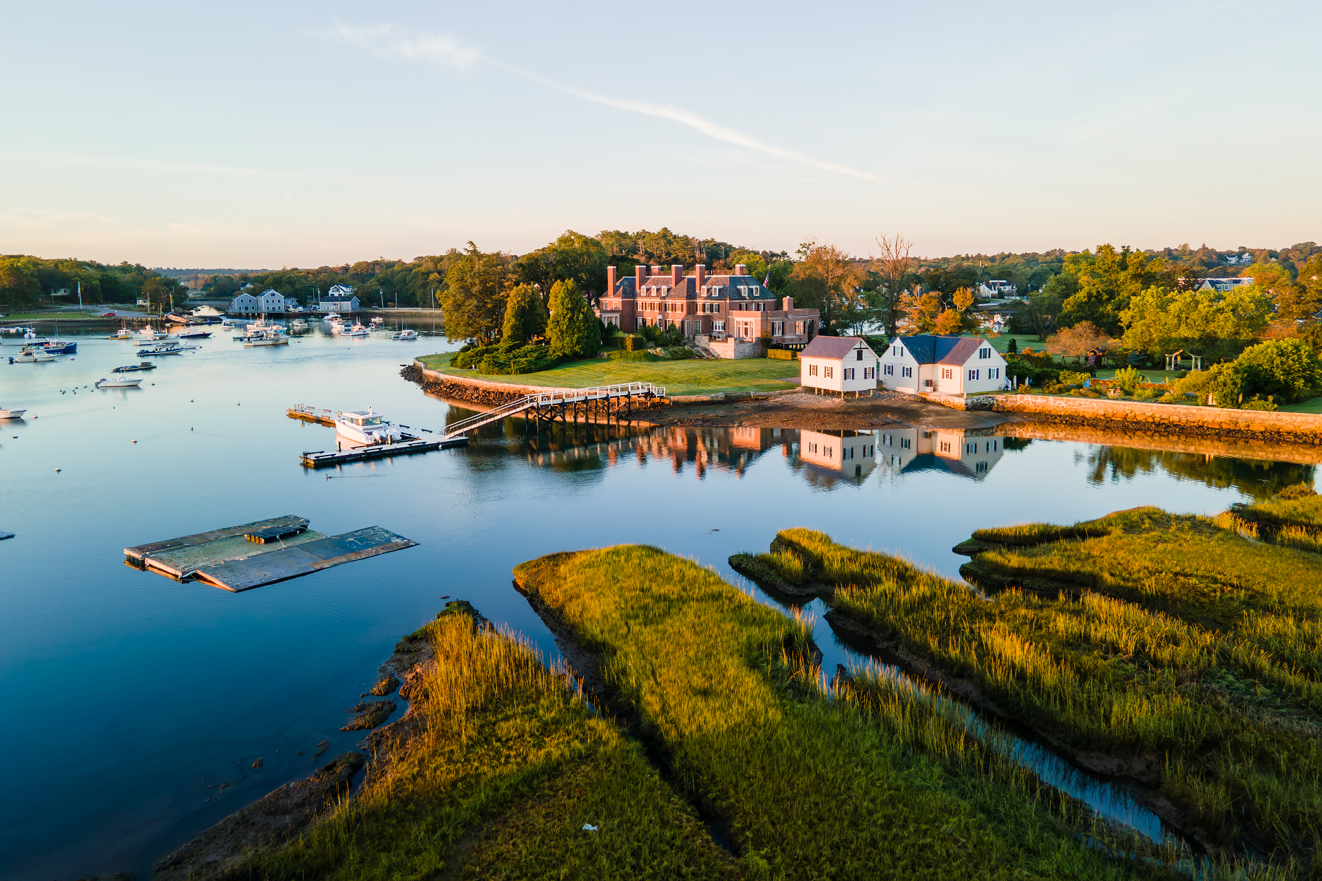 Aerial sunrise view of Cohasset Cove highlighting "The Oaks" estate, with calm water reflections and golden marsh grass.