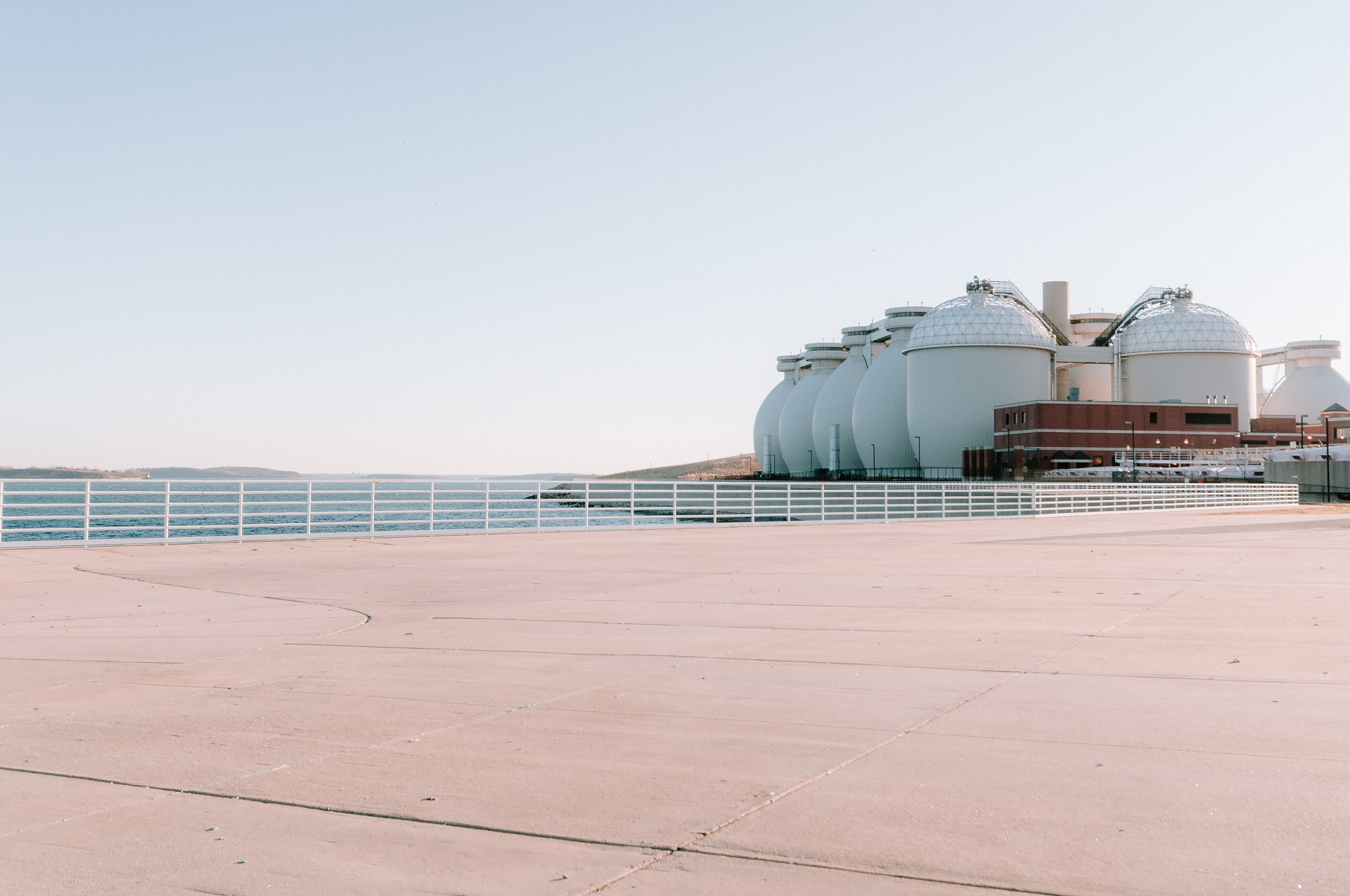 Wide view of Deer Island and its sludge digesters across calm harbor water under soft late-day light.