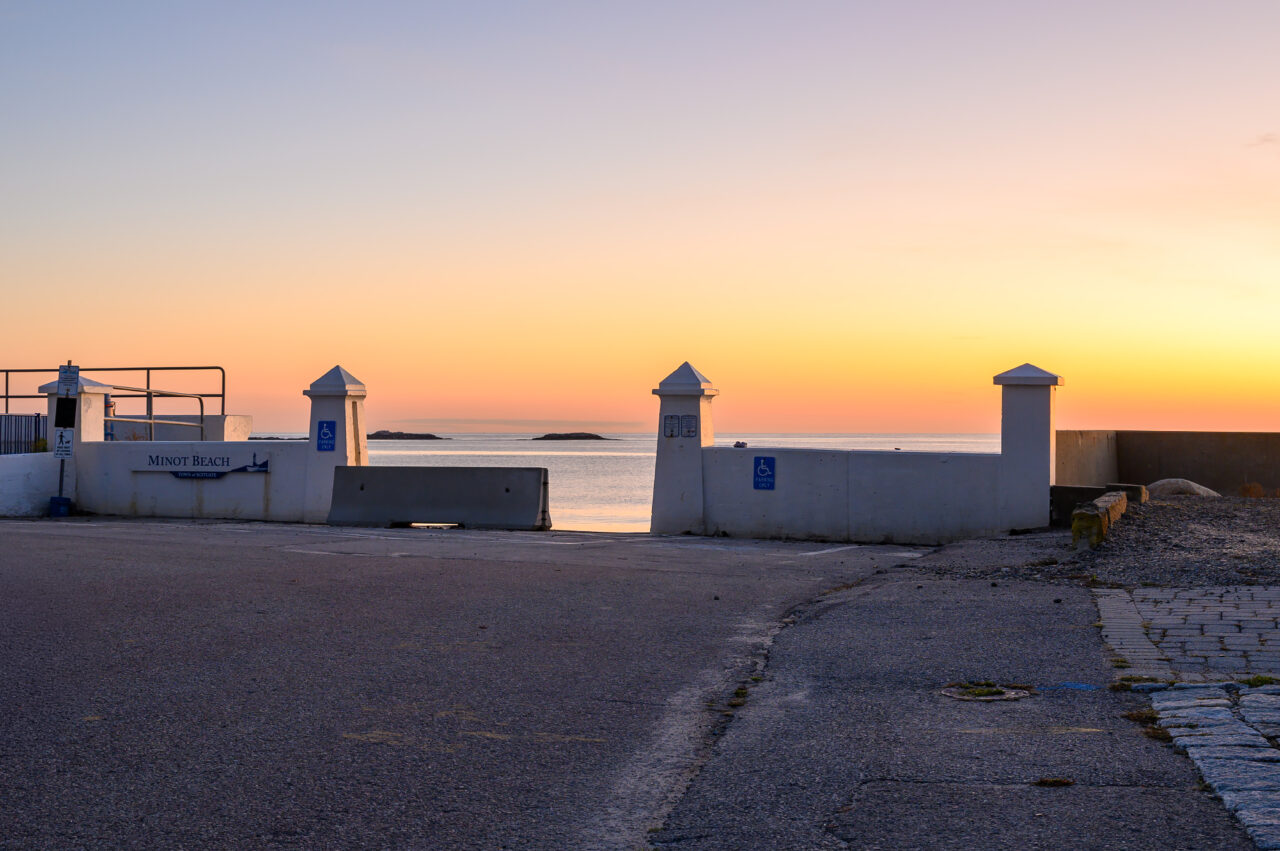 Concrete pillars and a seawall marking the Minot Beach entrance during sunrise.