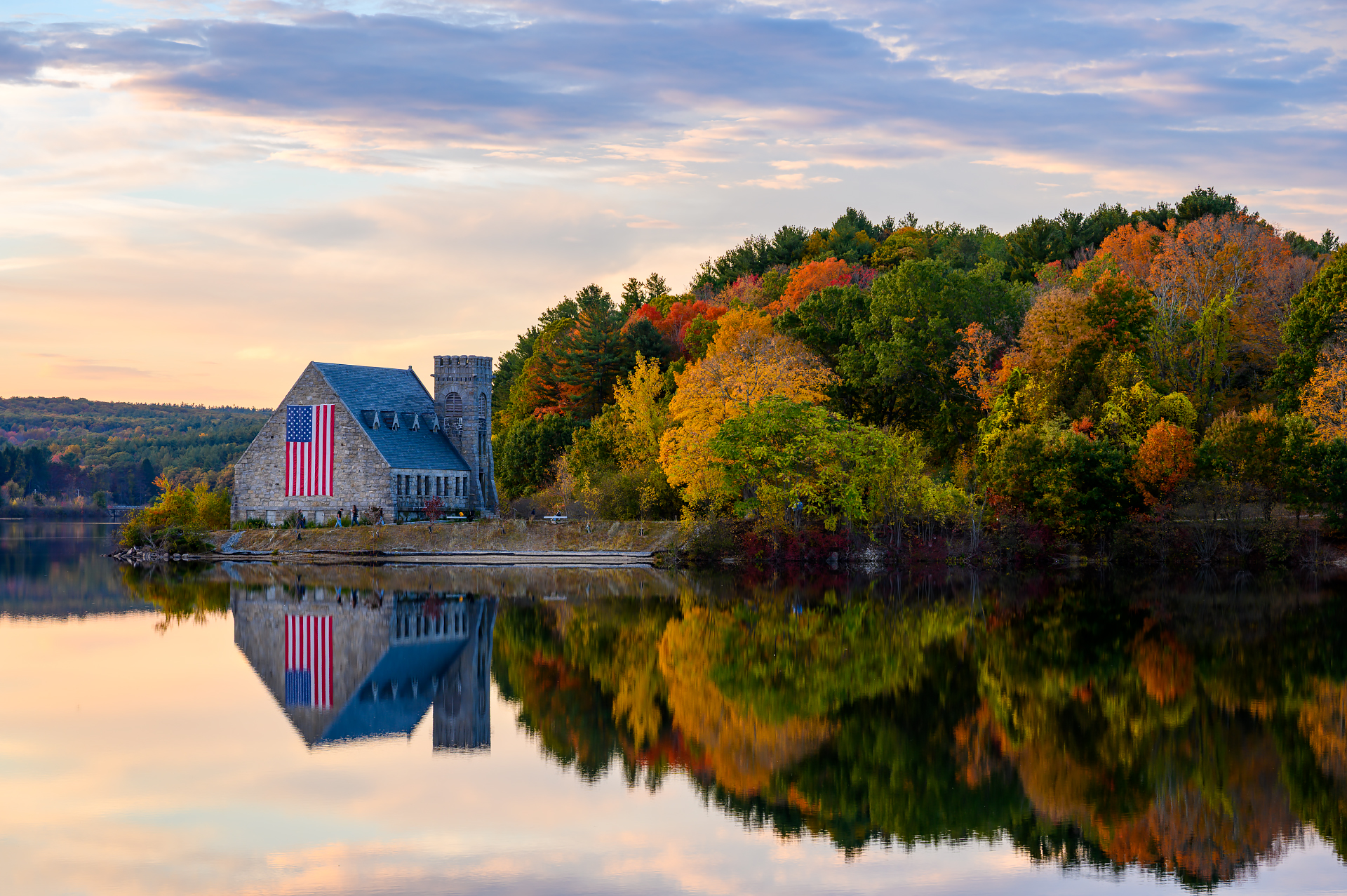 Twilight view of the Old Stone Church in autumn, with the illuminated flag vividly reflected in the dark water.