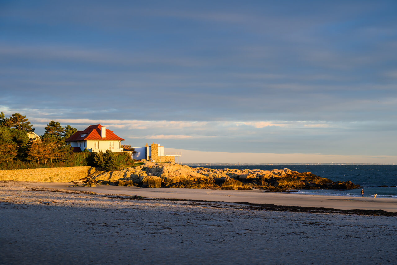 A house with a red roof perched on a cliff near Sandy Beach in Cohasset at sunrise.