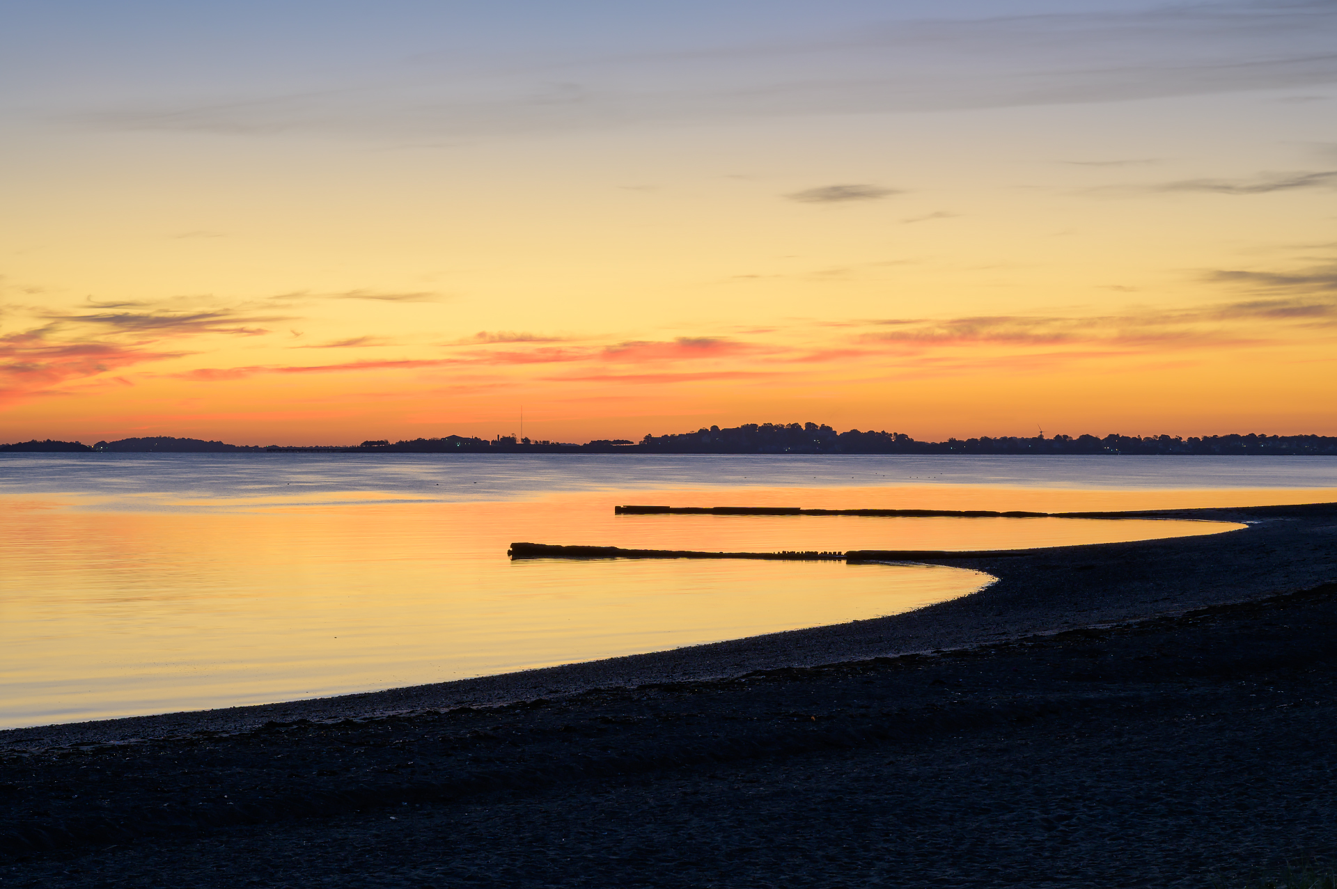 Golden light on the calm water at Wollaston Beach sunrise, with two groynes visible.