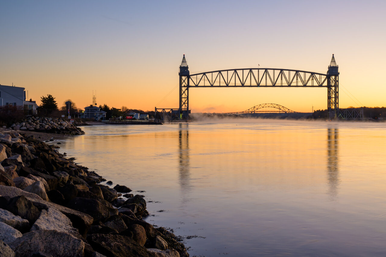 A rocky shore leading to the Cape Cod Canal Railroad Bridge just before sunrise.