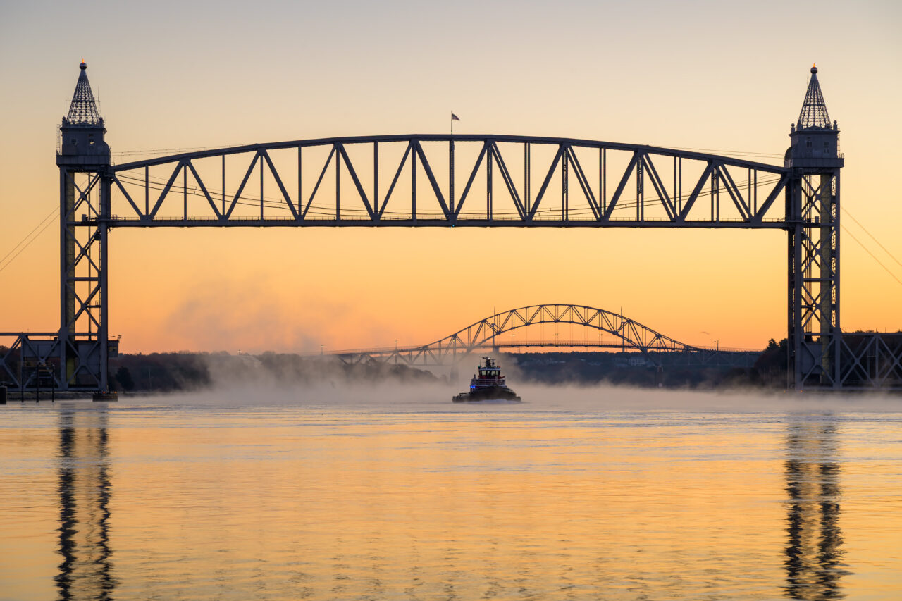 A tugboat moves slowly beneath the Cape Cod Railroad Bridge just before sunrise.