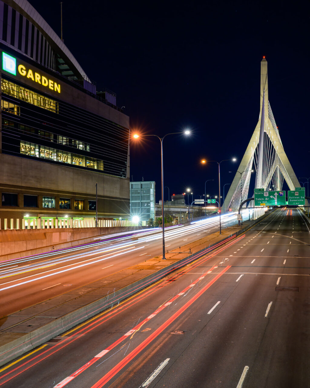 Long-exposure light trails on I-93 toward the Zakim Bridge, with TD Garden on the left, seen from Causeway Street near Portal Park.