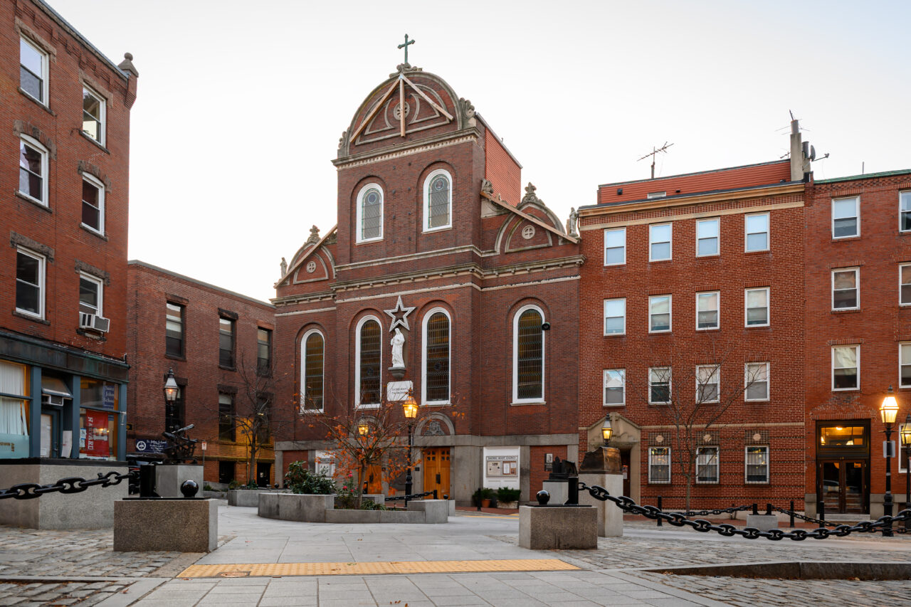The exterior of the red-brick Sacred Heart Church, centered in a cobblestone plaza in the North End neighborhood.