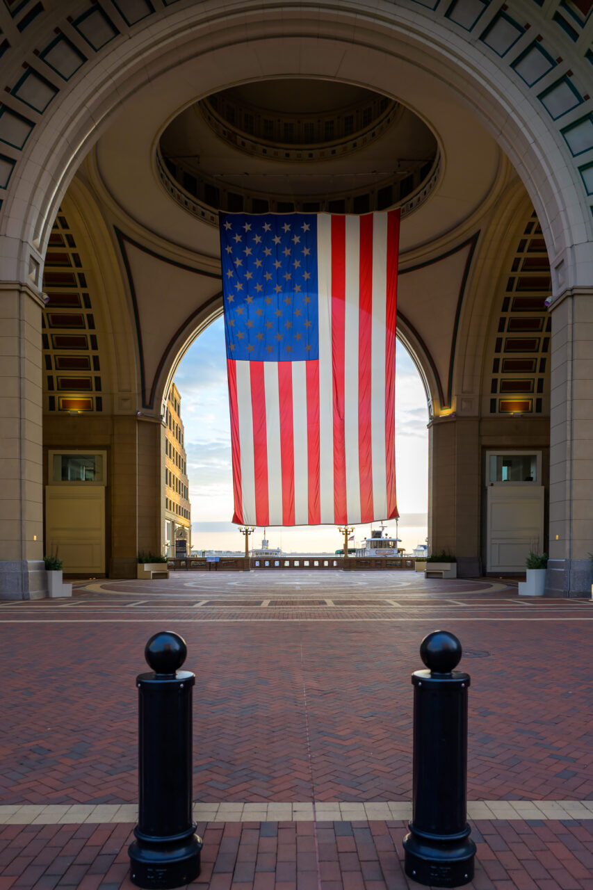 The large American flag hanging in the grand archway of the Boston Harbor Hotel during the early morning hours.