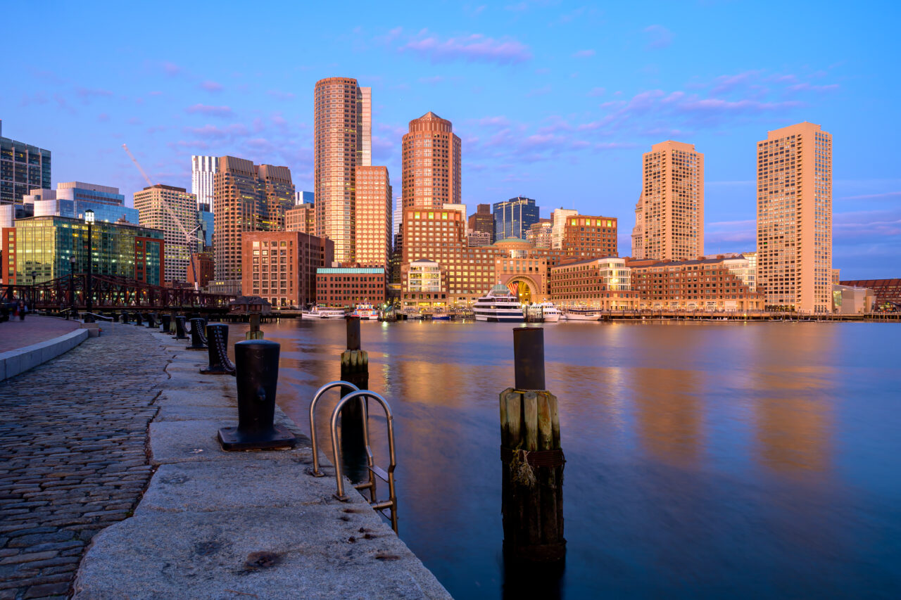 Long exposure photography of the Boston waterfront during the blue hour with smooth, glass-like water.