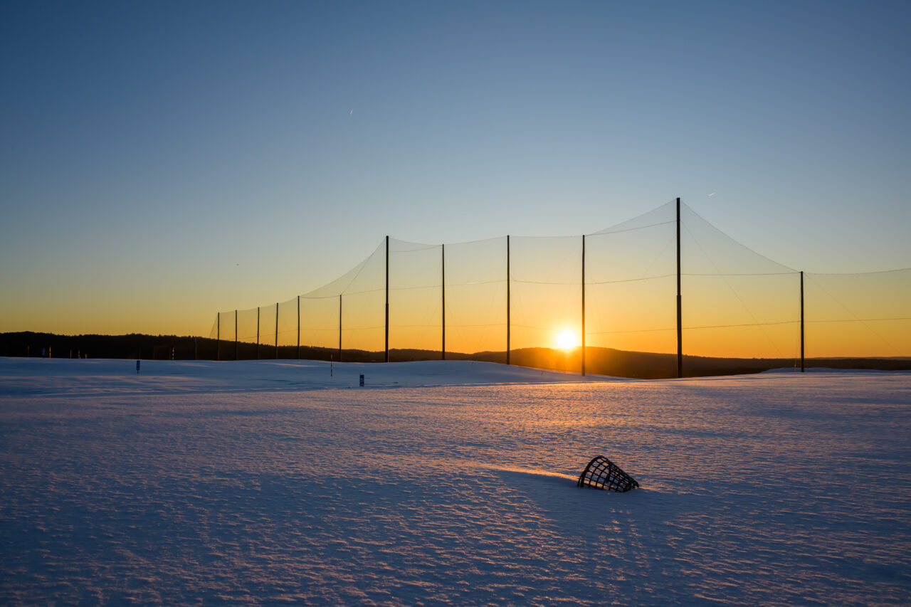 A quiet sunset over the snow-covered practice field at Granite Links, with a lone range bucket catching the golden light.