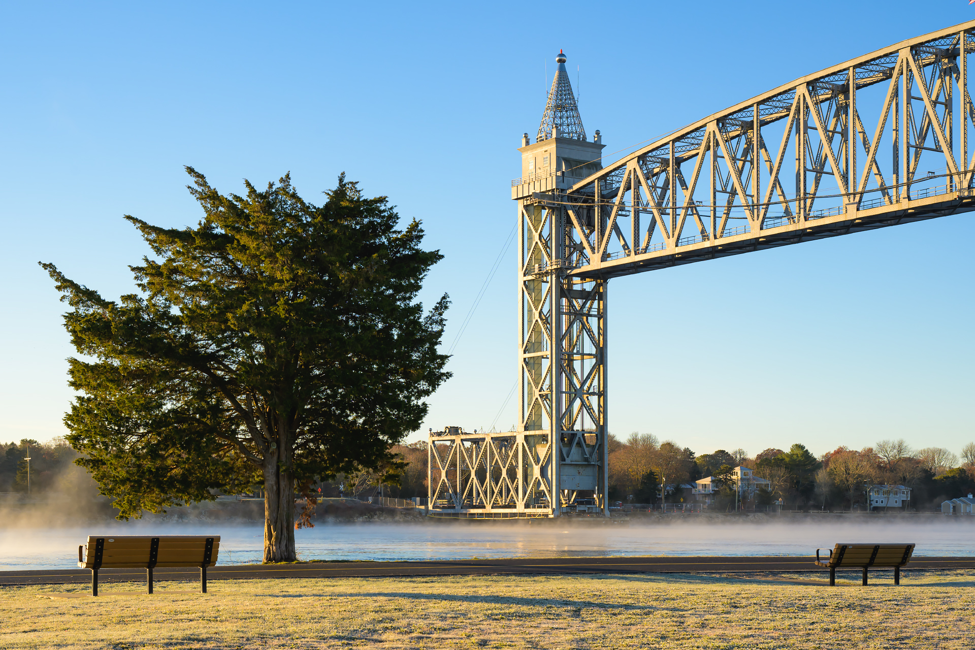 The Cape Cod Canal Railroad Bridge on a frosty morning, with early sunlight melting frost and casting soft light over the structure and surrounding landscape.