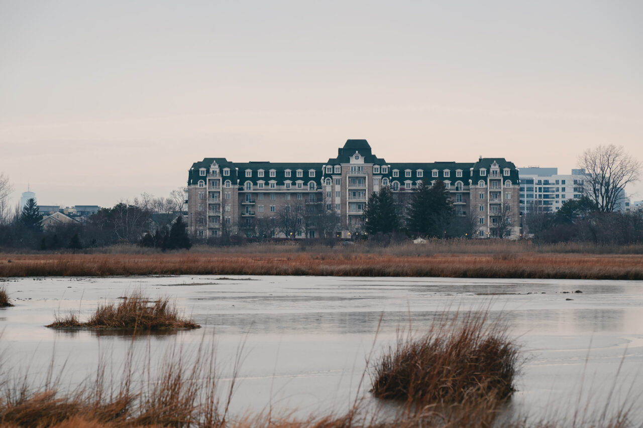 A grand residential manor building stands behind a partially frozen marsh at Marina Bay in Quincy, Massachusetts.