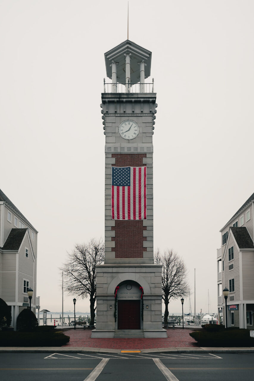 The Vietnam Veterans Memorial Clock Tower at Marina Bay in Quincy, featuring a large American flag draped over its stone facade.