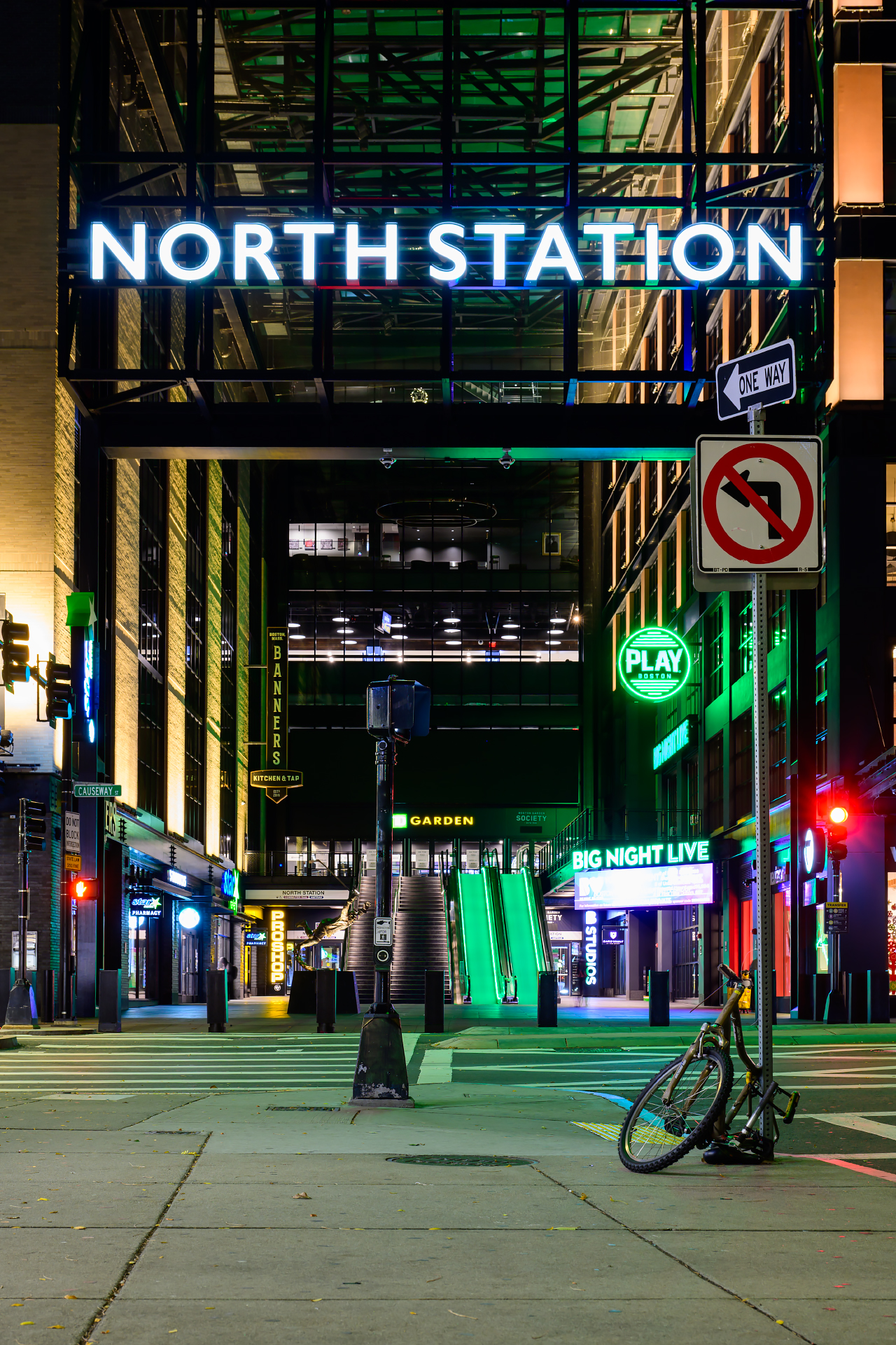 A vibrant night shot of the entrance to North Station in Boston, where the iconic "NORTH STATION" sign glows in bright white against a dark industrial frame.