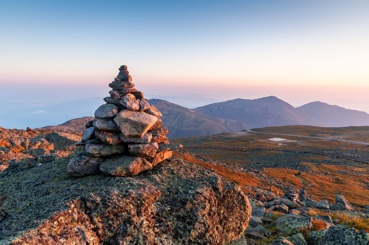 Stone cairn atop Mount Washington overlooking the White Mountains at sunrise.