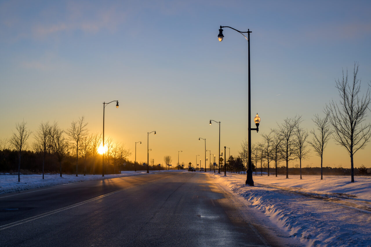 A view of Bill Delahunt Parkway heading west during golden hour, with the sun setting over the former South Weymouth Naval Air Station.