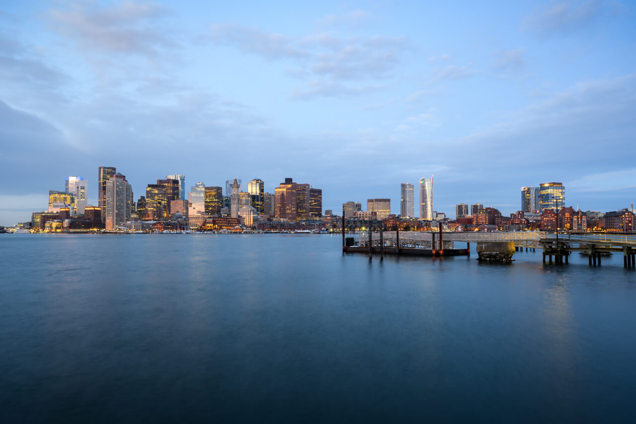 The Boston skyline glowing at blue hour, seen from Lewis Mall Wharf in East Boston.