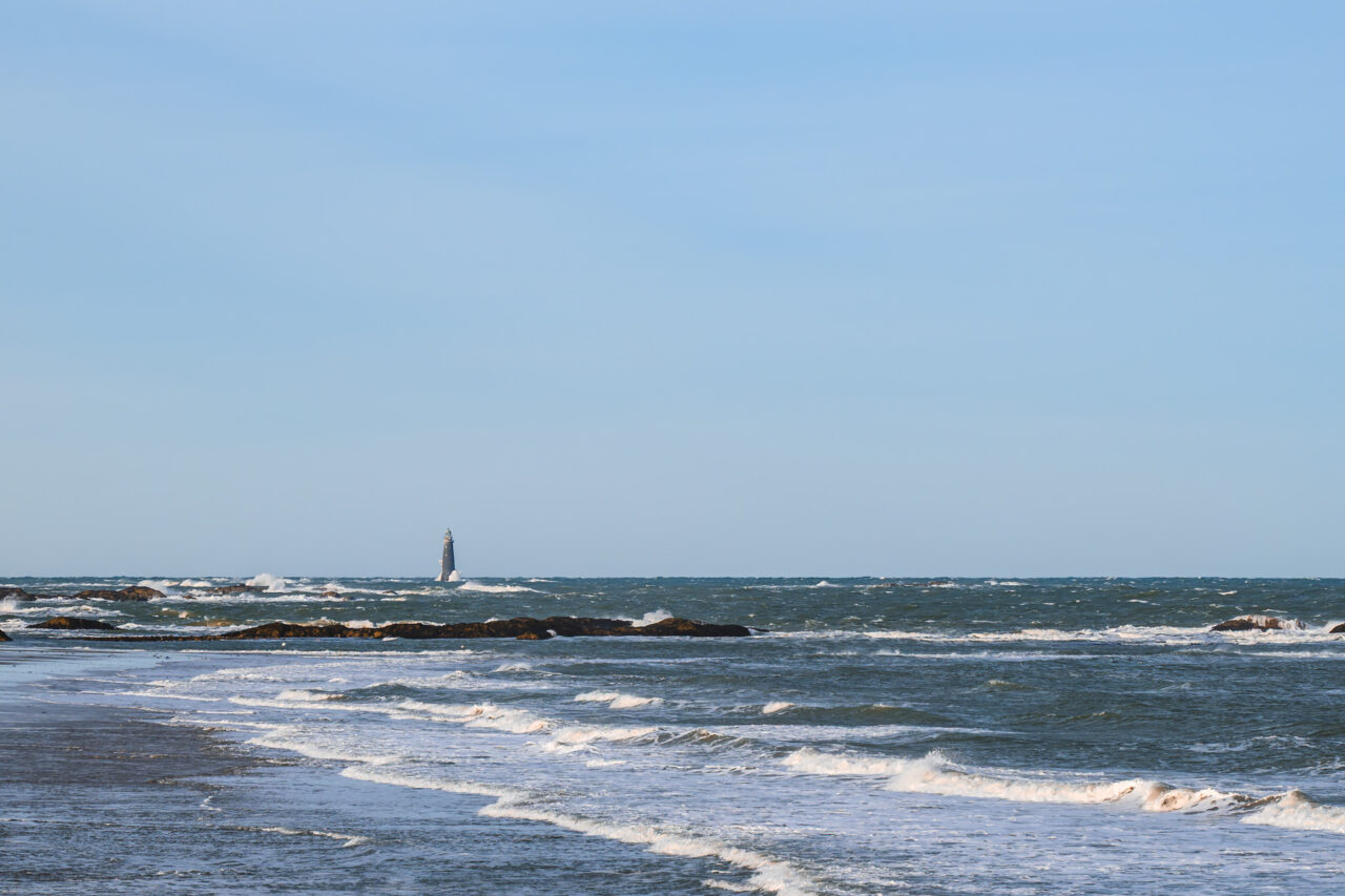 The distant silhouette of Minot's Ledge Light surrounded by white-capped winter swells.