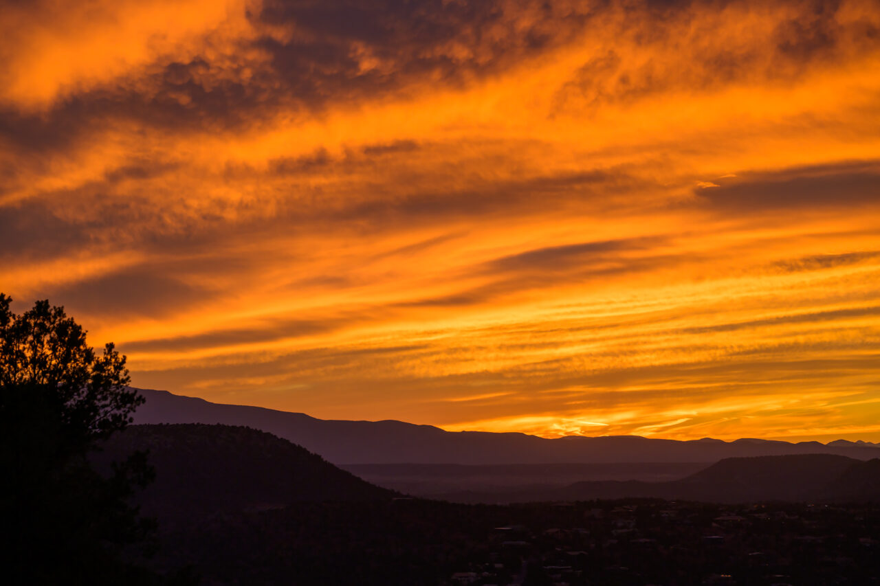 Dramatic orange and gold clouds stretching over the dark mountain silhouettes at Airport Mesa in Sedona.