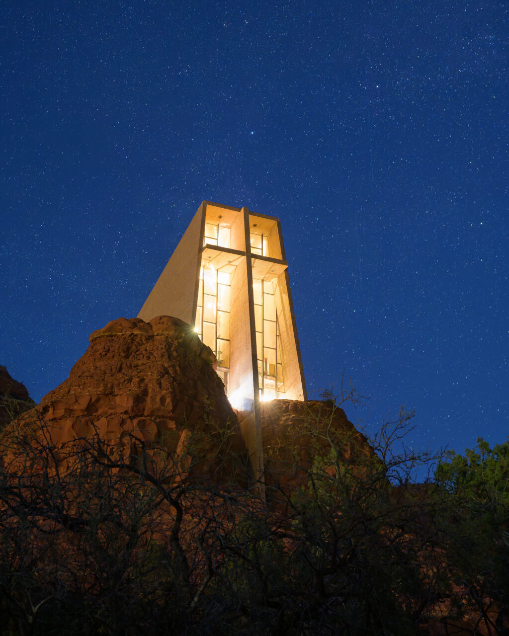 The Chapel of the Holy Cross illuminated at night under a starry sky in Sedona.